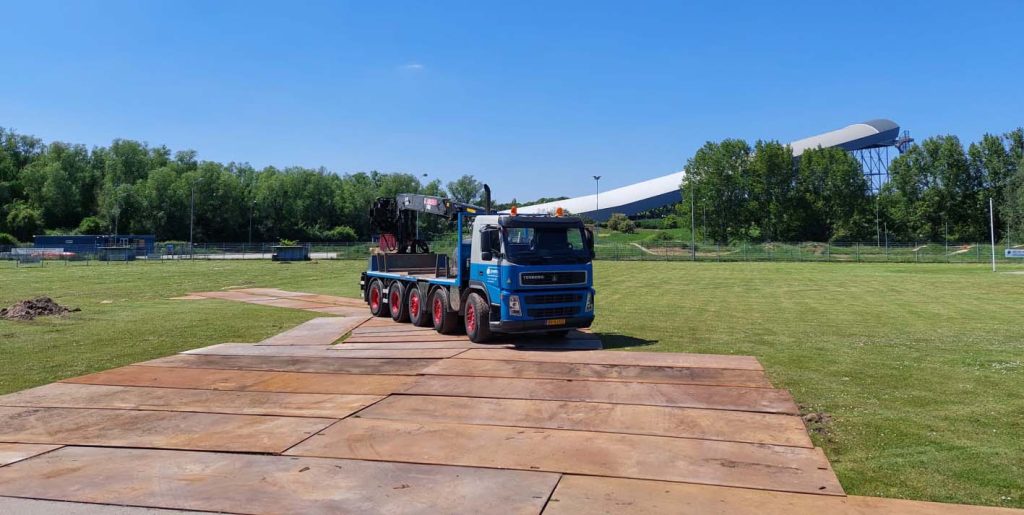 Een blauwe vrachtwagen op rijplaten op een grasveld